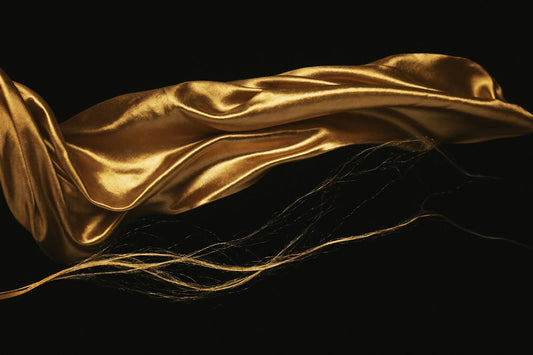 Flowing gold silk fabric on black — satin vs silk for hair and skin