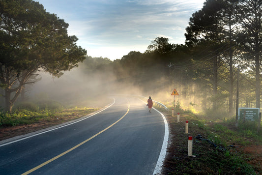 A solitary figure walking forward along a foggy, winding road at dawn