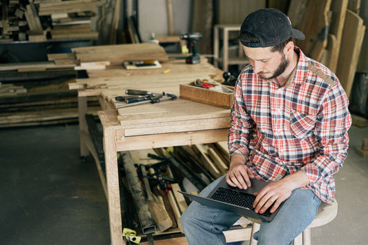 A craftsman using a laptop in his woodworking workshop