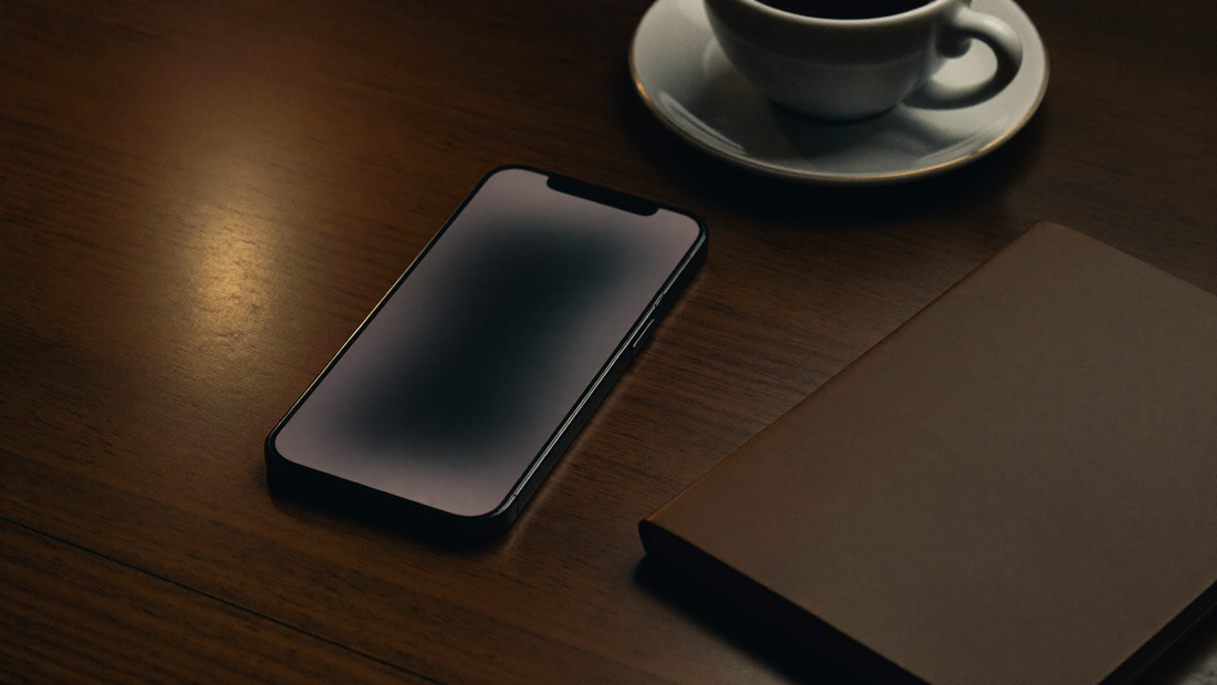 A smartphone with a dark, unreadable screen on a walnut desk, showing how a privacy screen protector blocks side viewing